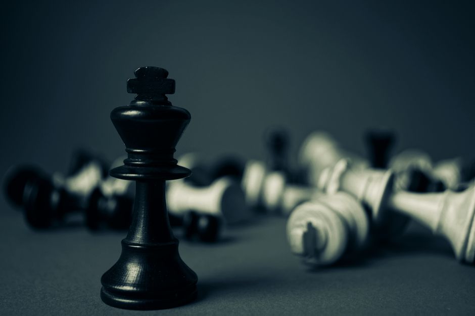 Black king chess piece stands tall among fallen pieces, symbolizing strategy and triumph.