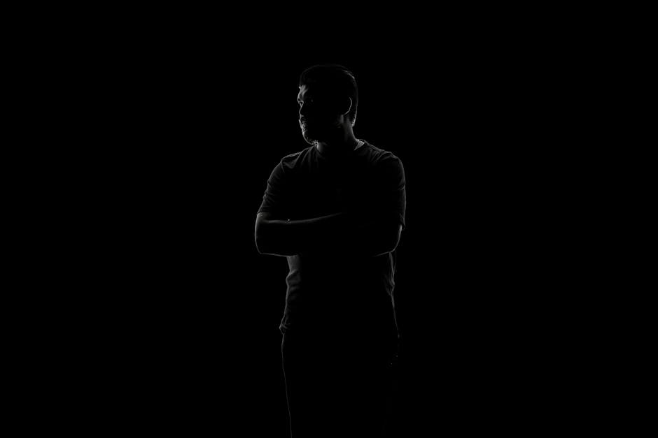 A captivating silhouette of a man standing with arms crossed against a black background, evoking mystery.