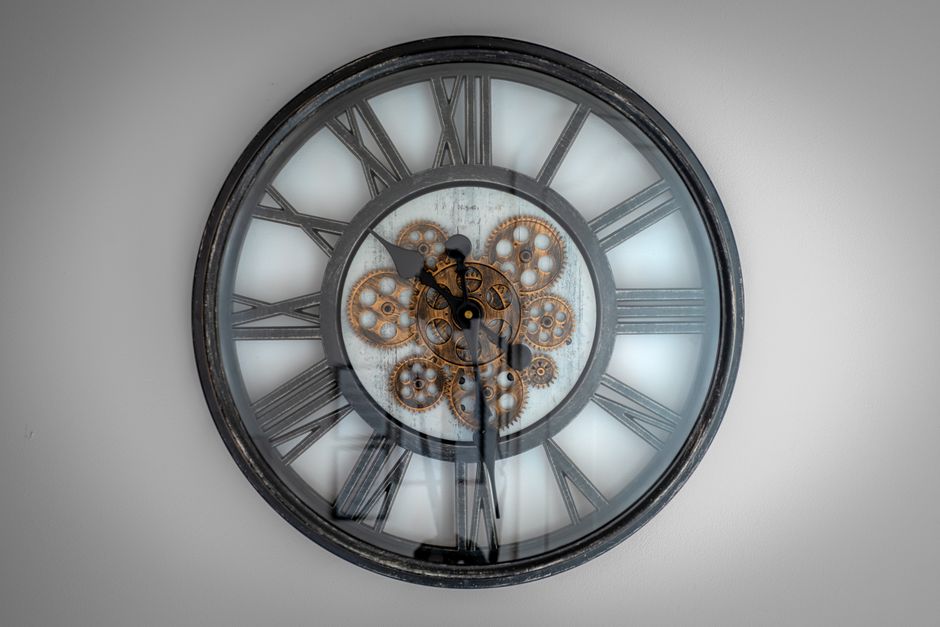 Close-up of a vintage Roman numeral wall clock with visible gears and metal frame.