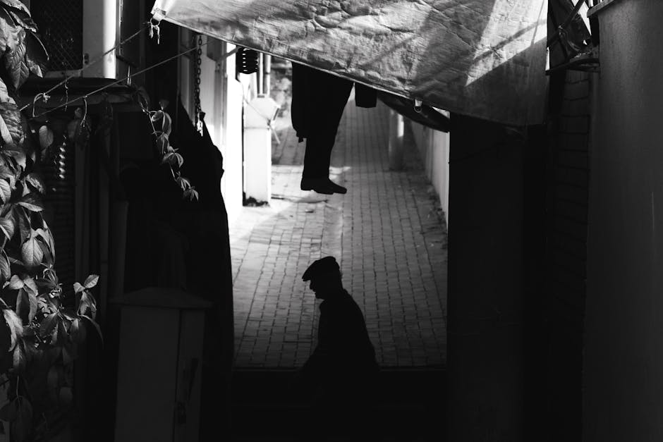 Silhouette of an elderly man standing in a narrow urban alley, creating a moody, dramatic scene.