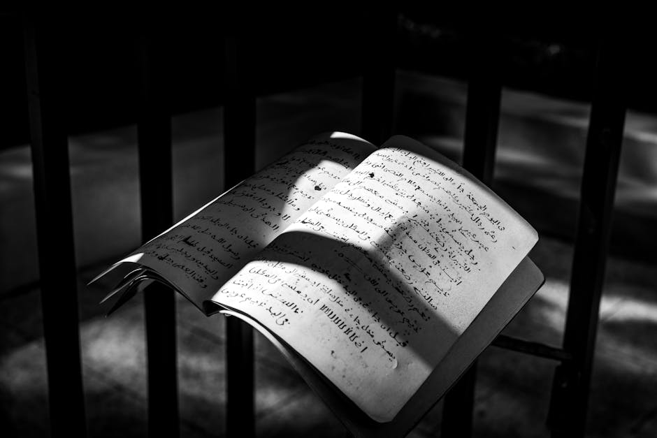 Monochrome image of an open book in sunlight and shadows, featuring handwritten text.