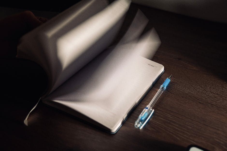 A notebook with turning pages and a pen on a wooden desk in low light.