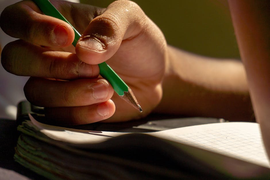 Detailed view of a hand writing with a pencil in a notebook, implying study or creativity.