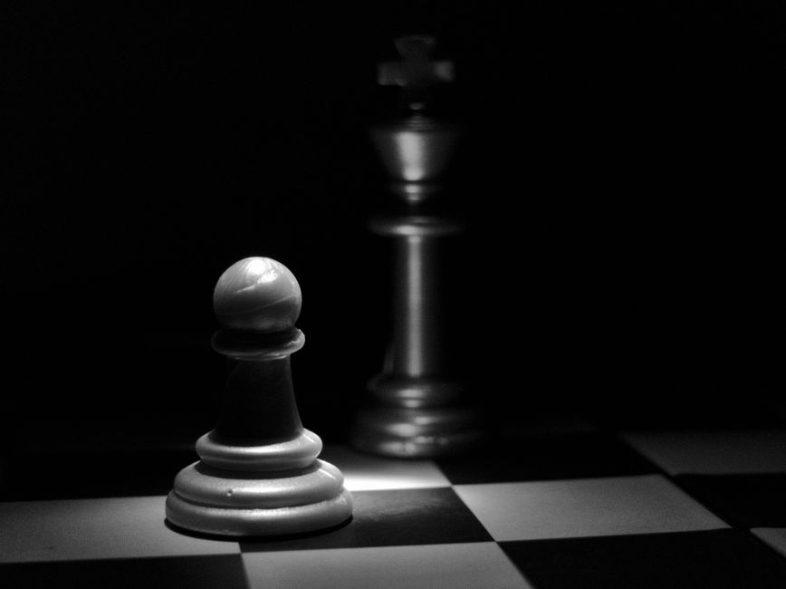 A dramatic black and white photo of chess pieces with intense lighting and shadows.