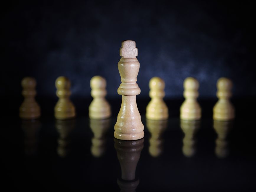 Close-up view of a wooden chess king and pawns on a reflective black surface.