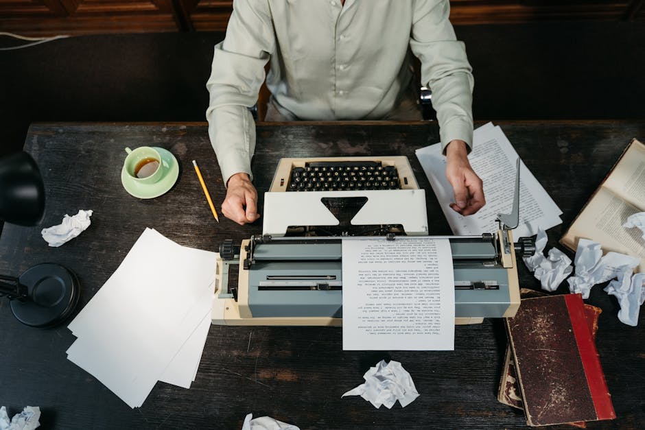 An overhead view of a workspace with a vintage typewriter, scattered papers, and a person writing.